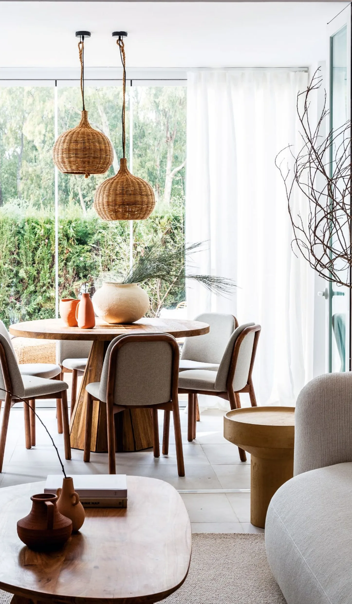 Round teak dining table with upholstered chairs and two woven pendant lamps